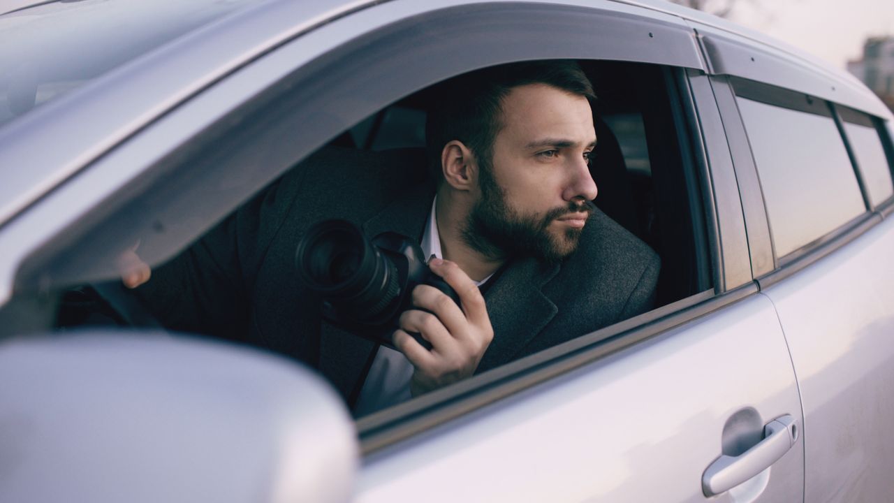 Man with a camera looking out of car window capturing a scene. Ideal for photography and exploration themes.