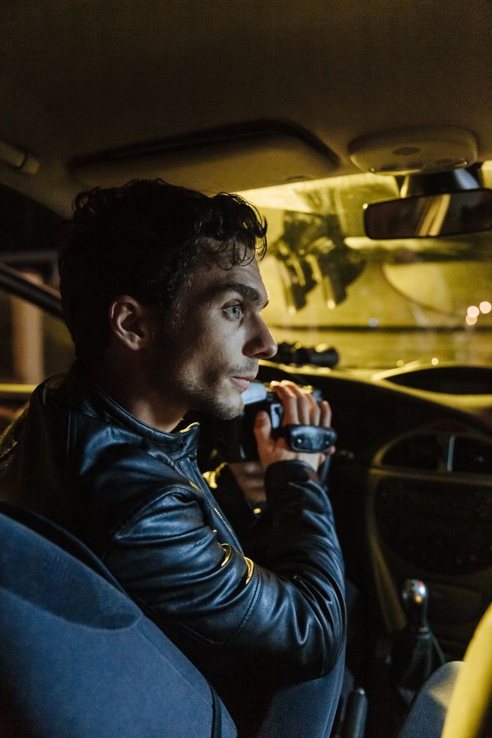 Man sitting in a car at night holding a camcorder, capturing hidden footage.
